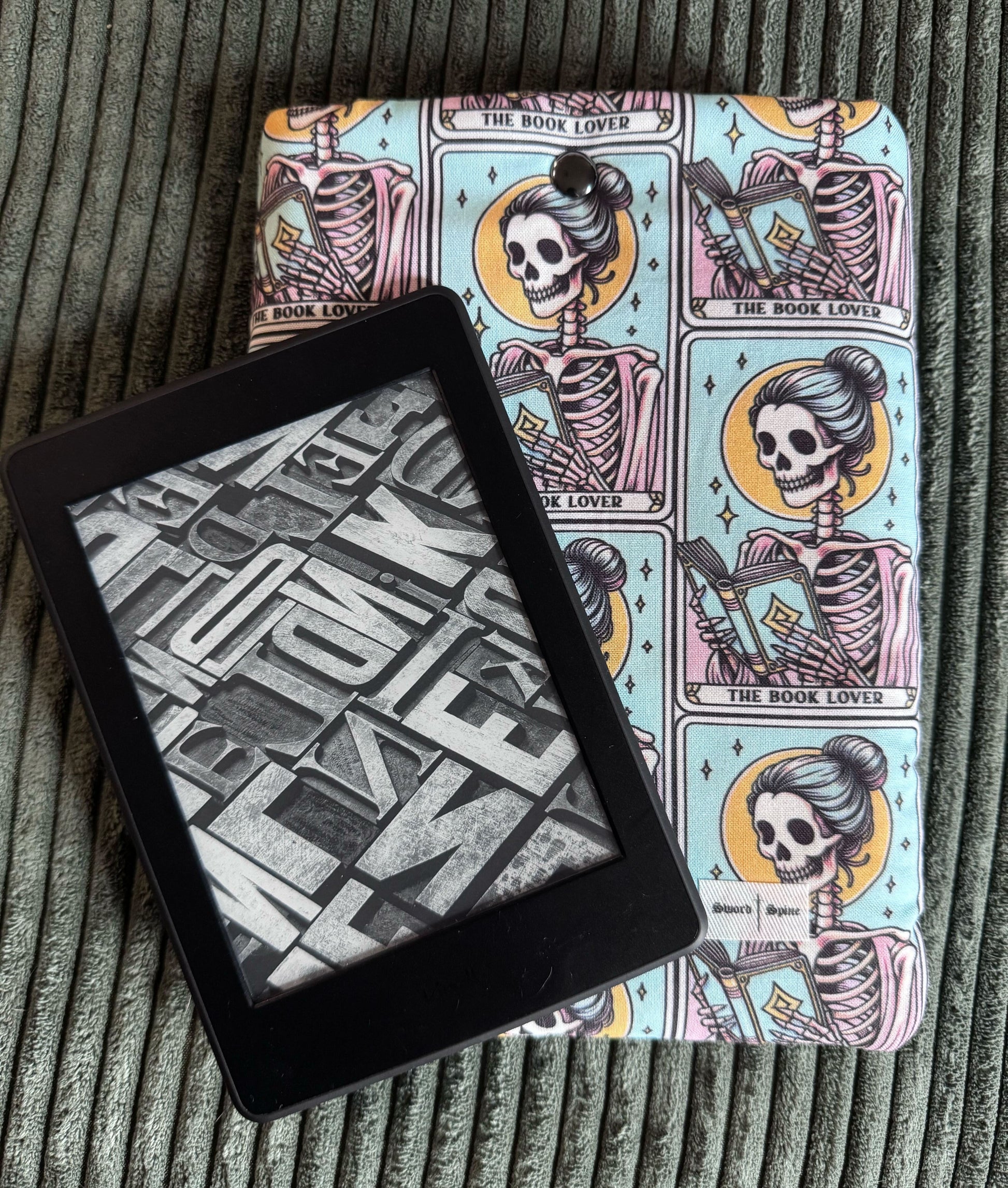 A kindle rests on top of a handmade e-reader sleeve with tarot cards featuring a woman reading.