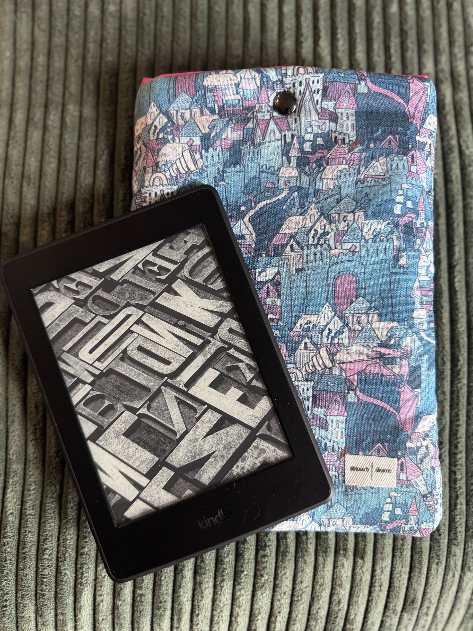 A kindle rests on top of a handmade e-reader sleeve with a castles and dragons pattern.