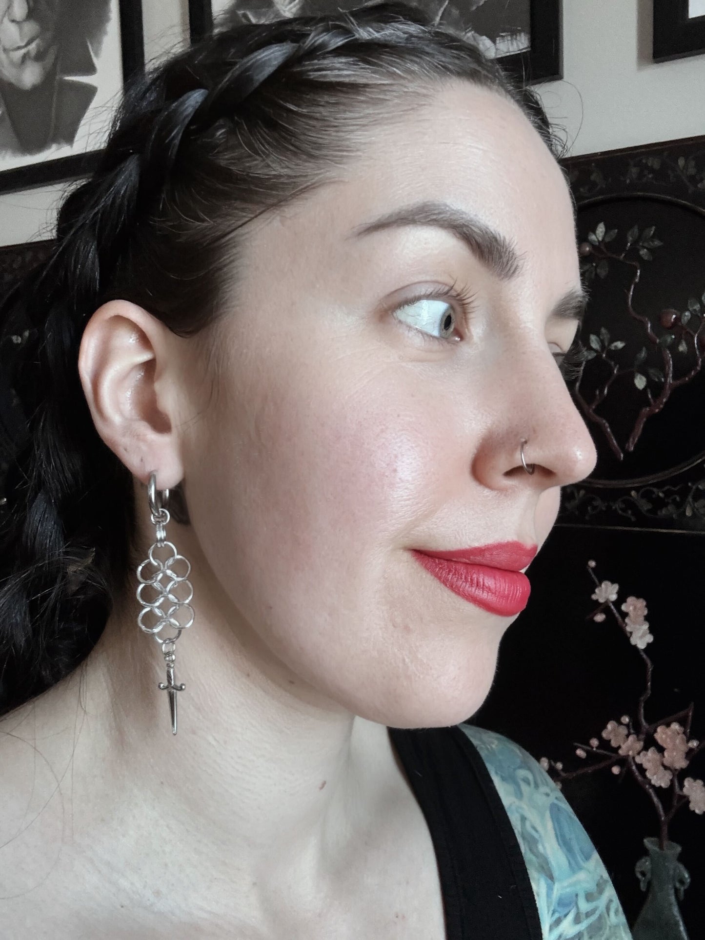 A woman wears a pair of European woven chainmail earrings with a dagger hanging at the bottom.