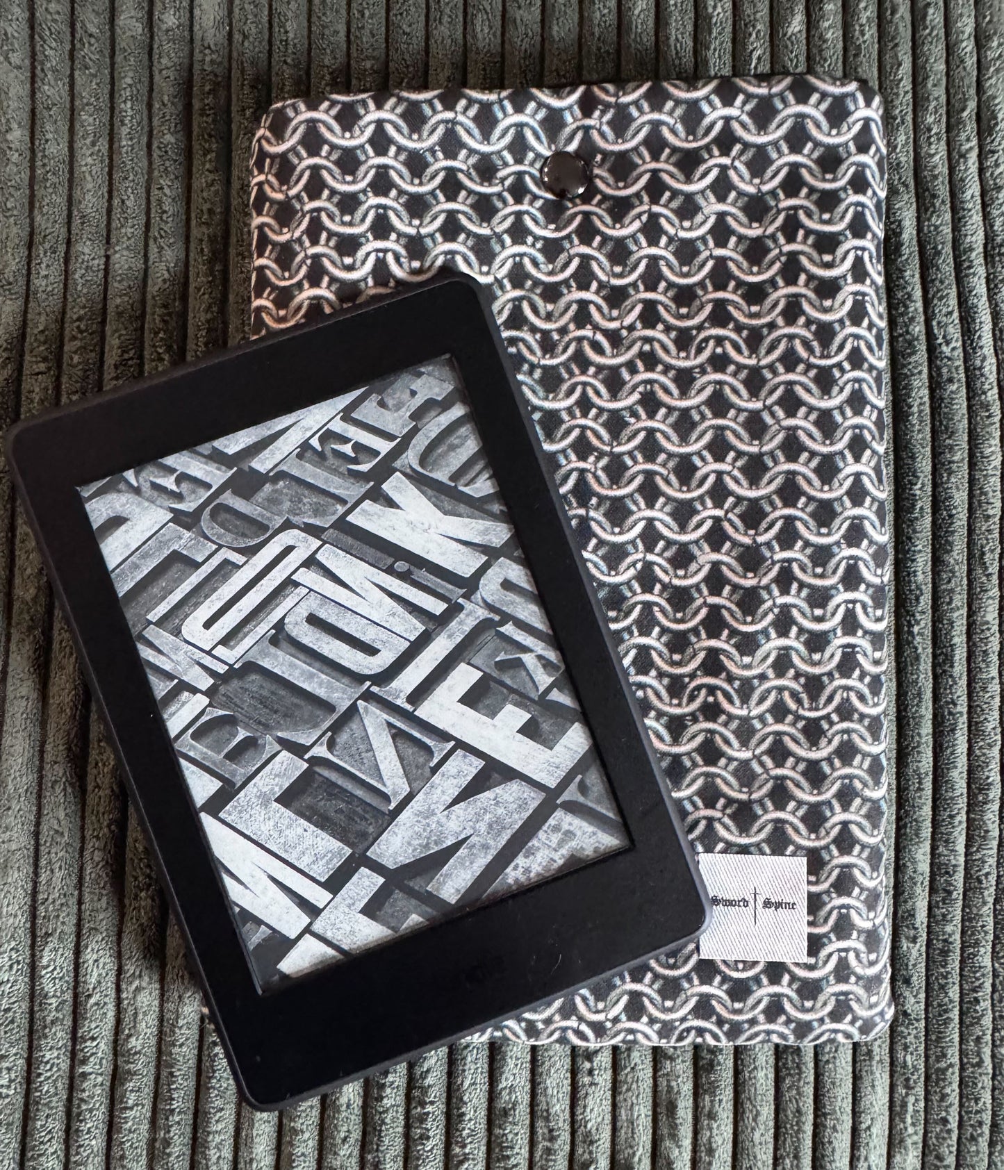 A kindle rests on top of a handmade e-reader sleeve featuring a chainmail pattern.