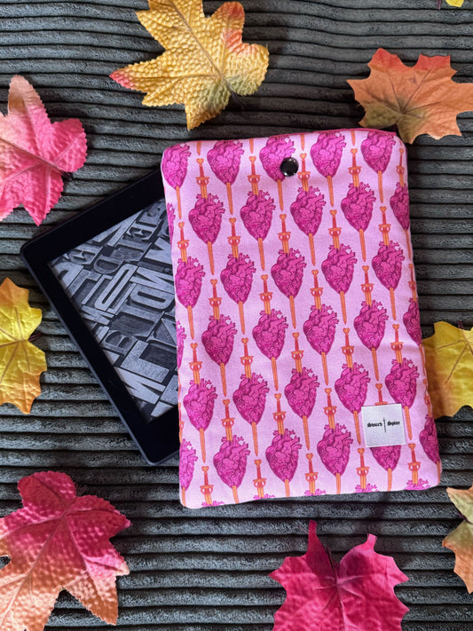A handmade kindle e-reader sleeve features a repeated pattern of hearts being pierced with swords.