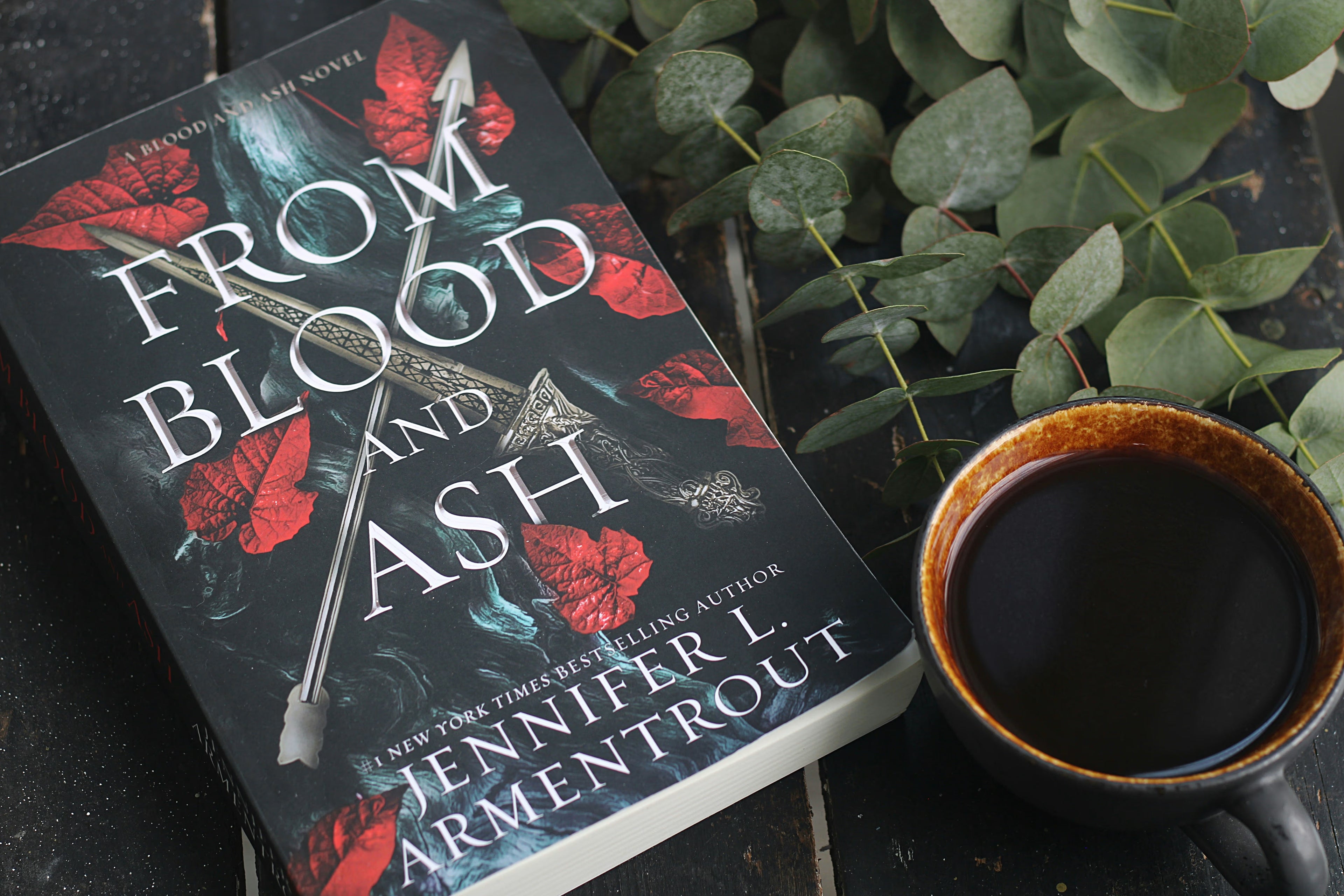 Fantasy romance book with the title of 'From Blood and Ash' on the cover displaying a dagger, arrow, and red leaves.