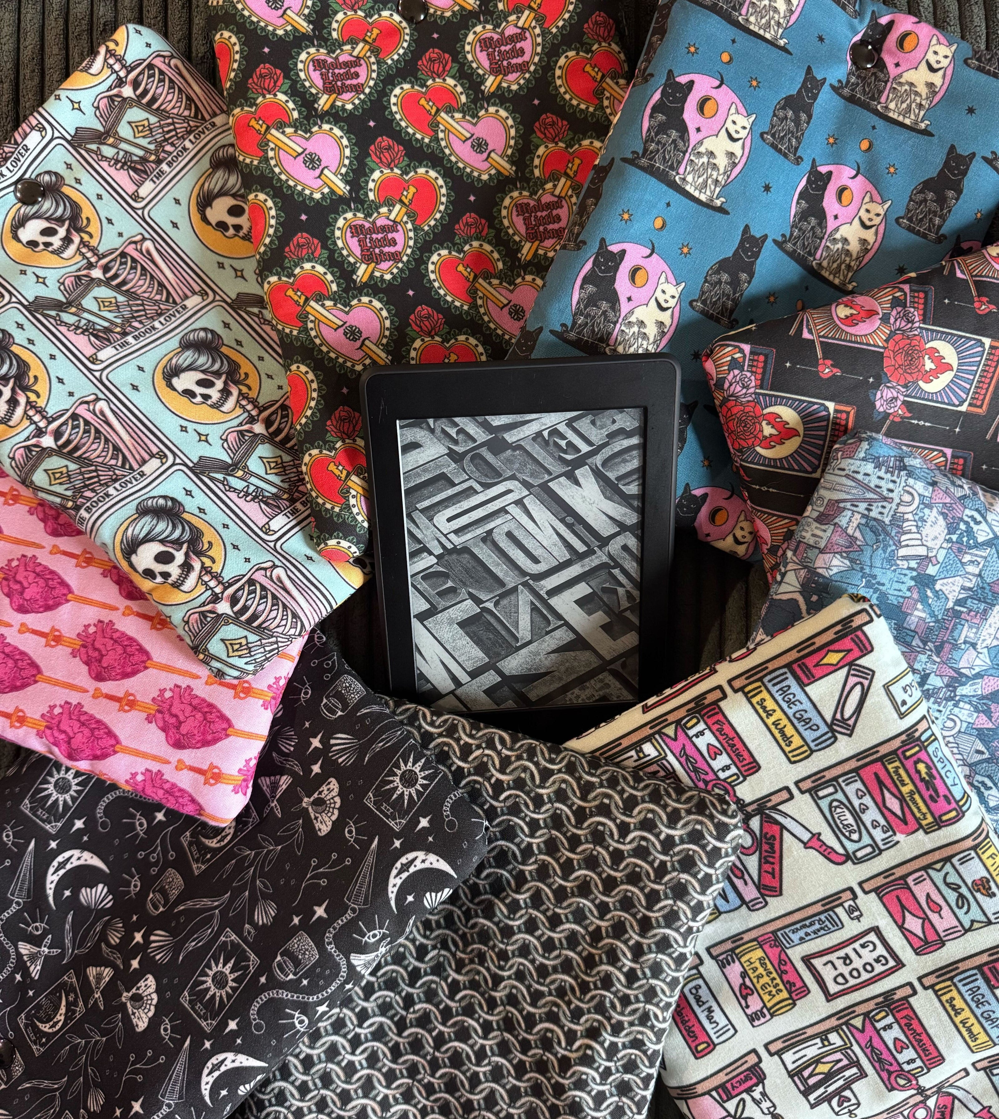 A kindle rests in the middle of several handmade kindle e-reader sleeves.
