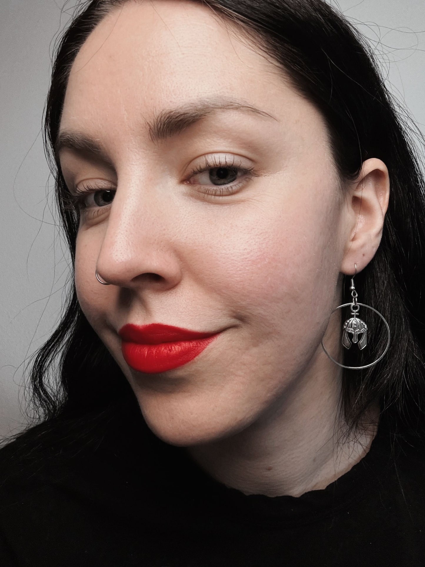 A woman wears a pair of hook earrings featuring silver hoops with a knight's helmet dangling in the middle.