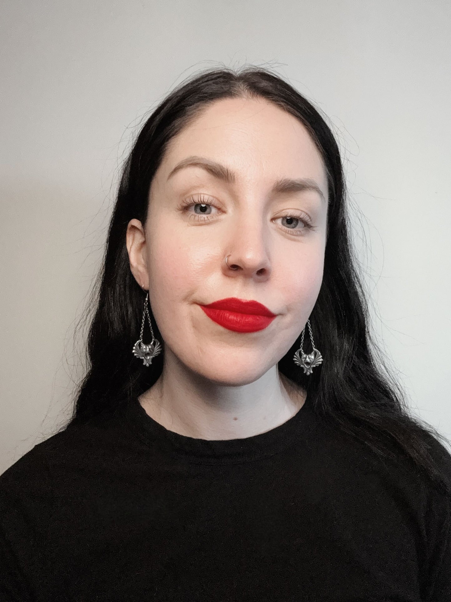 A woman wears a pair of gothic earrings featuring gargoyles hanging from chains.