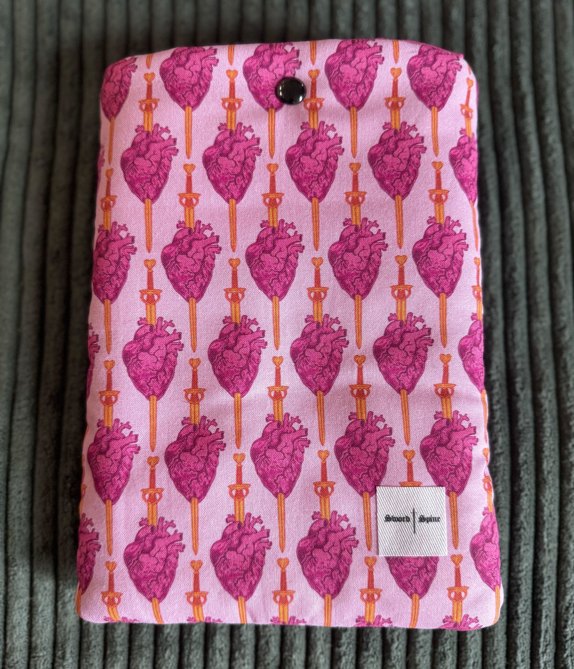 A pink handmade e-reader sleeve features a repeated pattern of hearts and swords.