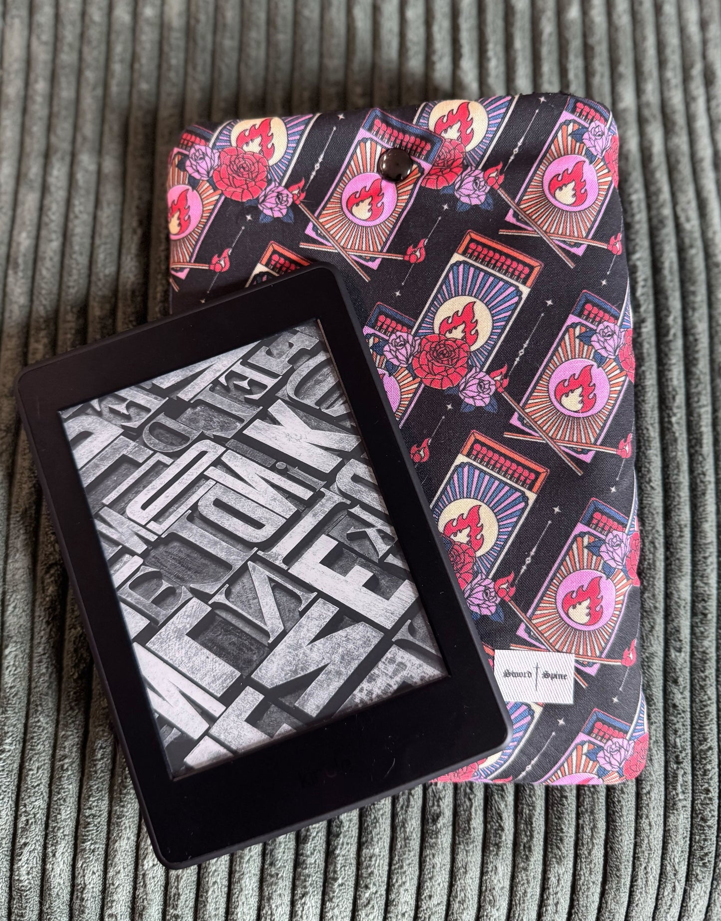 A kindle resting on a handmade e-reader sleeve with a repeating pattern of matchboxes.