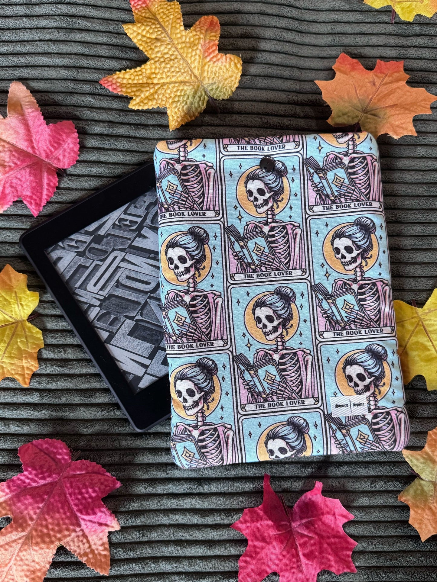 A handmade kindle e-reader sleeve features a repeated pattern of tarot cards with a woman reading.