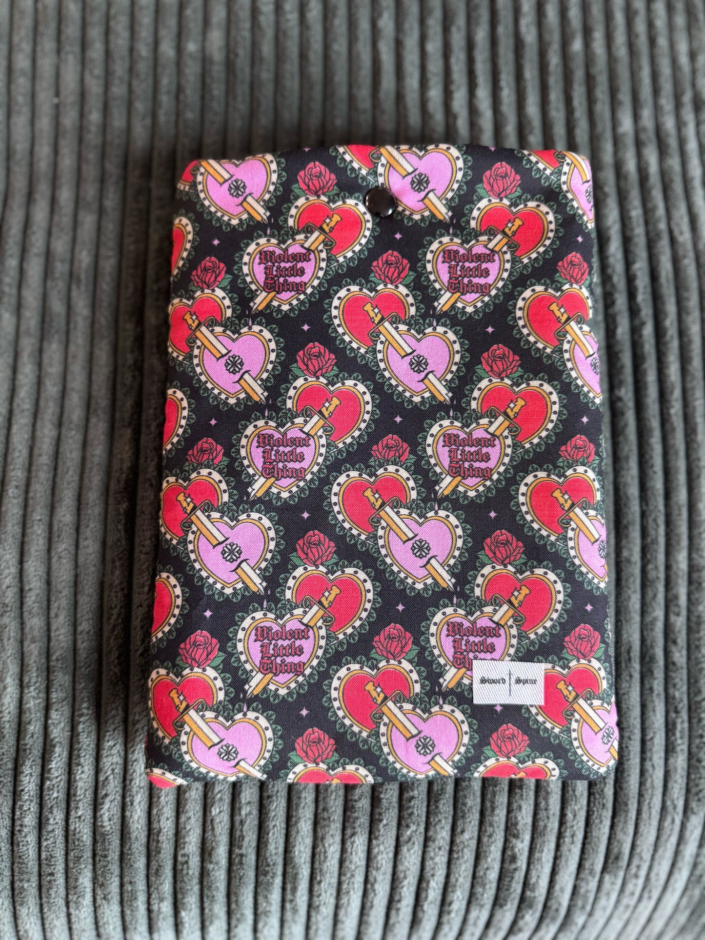 A coquette patterned kindle e-reader sleeve that says "Violent Little Thing" on hearts.