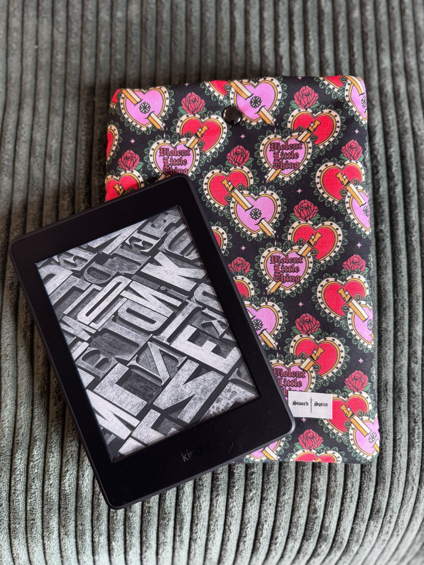 A kindle e-reader sleeve featuring a coquette heart design with a kindle resting on top.