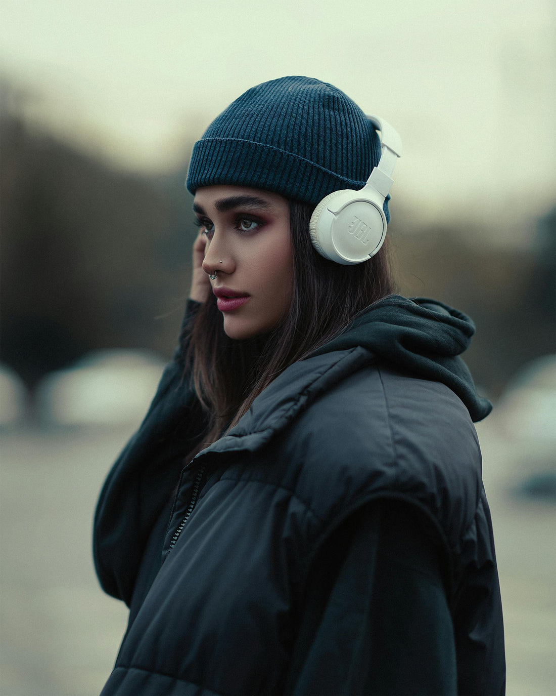 Woman in all black listening to her over the ear headphones.