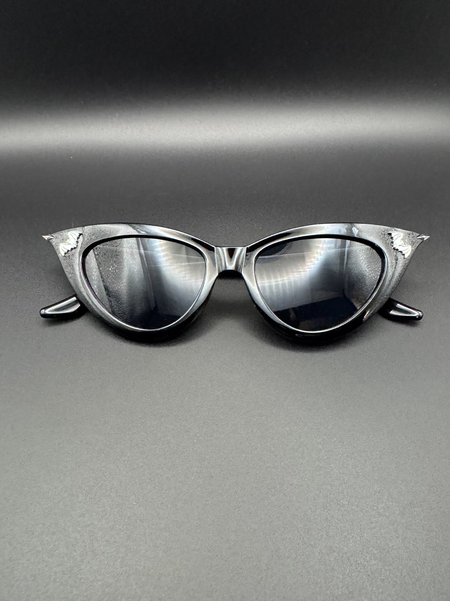 Black sunglasses with silver tips and bat decals rest on a dark background.