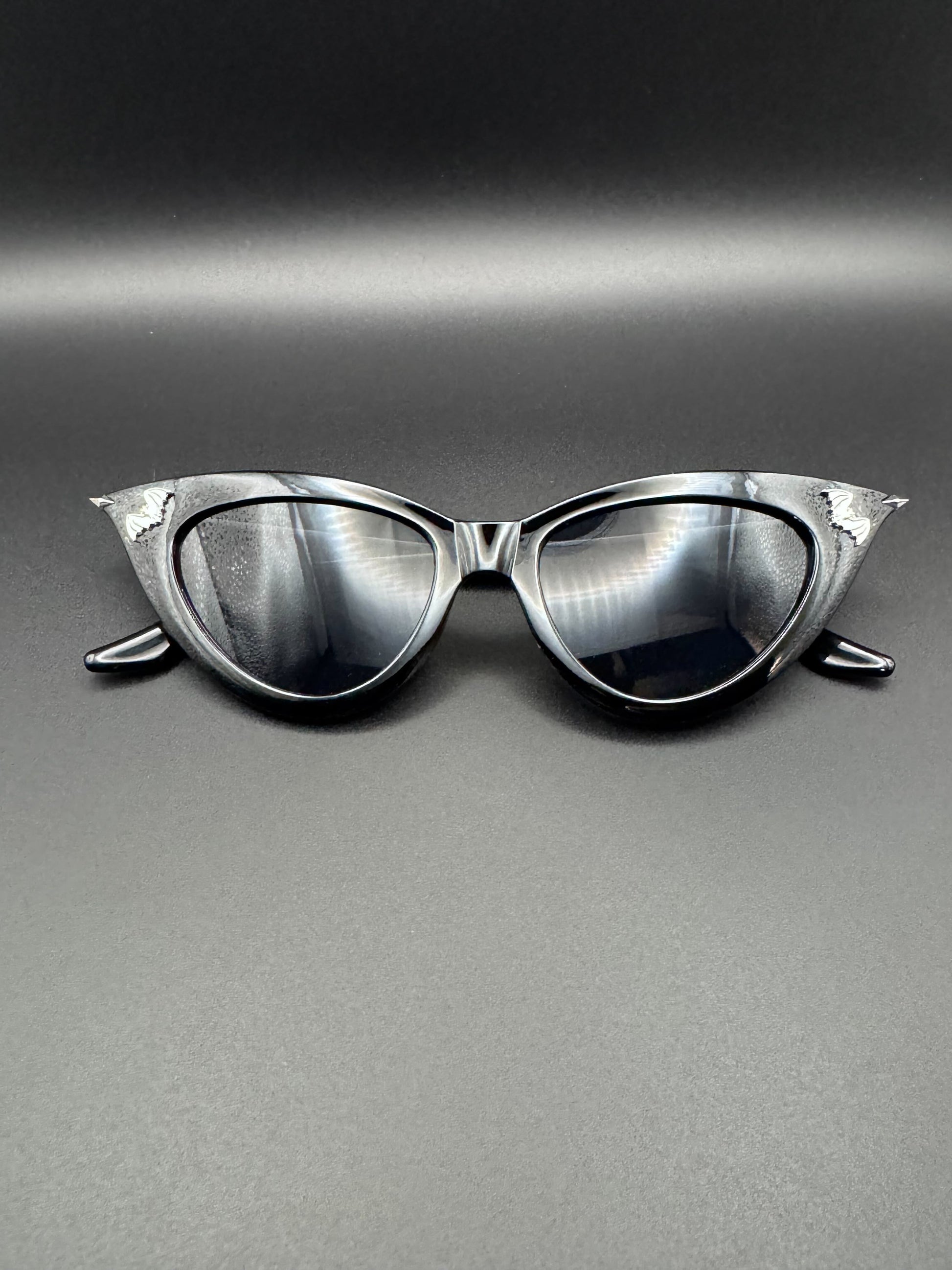 Black sunglasses with silver tips and bat decals rest on a dark background.