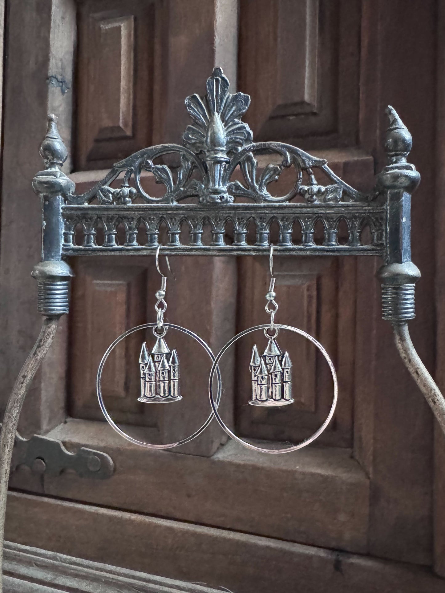 Castle charms hang inside of hoop earrings with a gothic cabinet in the background.