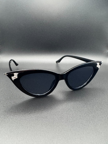 Cateye sunglasses with silver spike tips and bat decor, rest on a dark background.