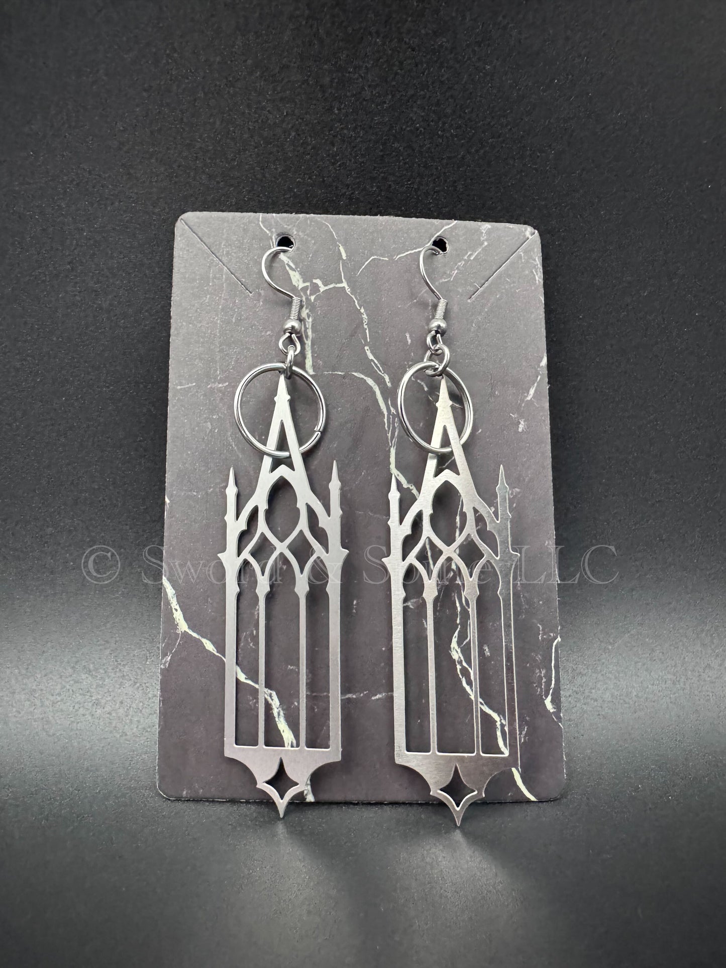 A pair of dramatic gothic cathedral window earrings displayed on a dark jewelry card.