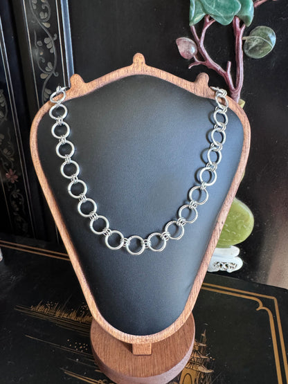 A delicate silver chainmail necklace rests on a display.