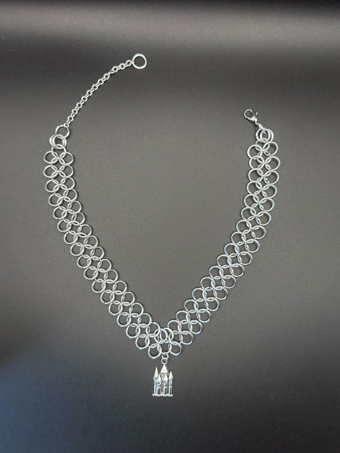 A silver chainmail choker with a medieval castle pendant.