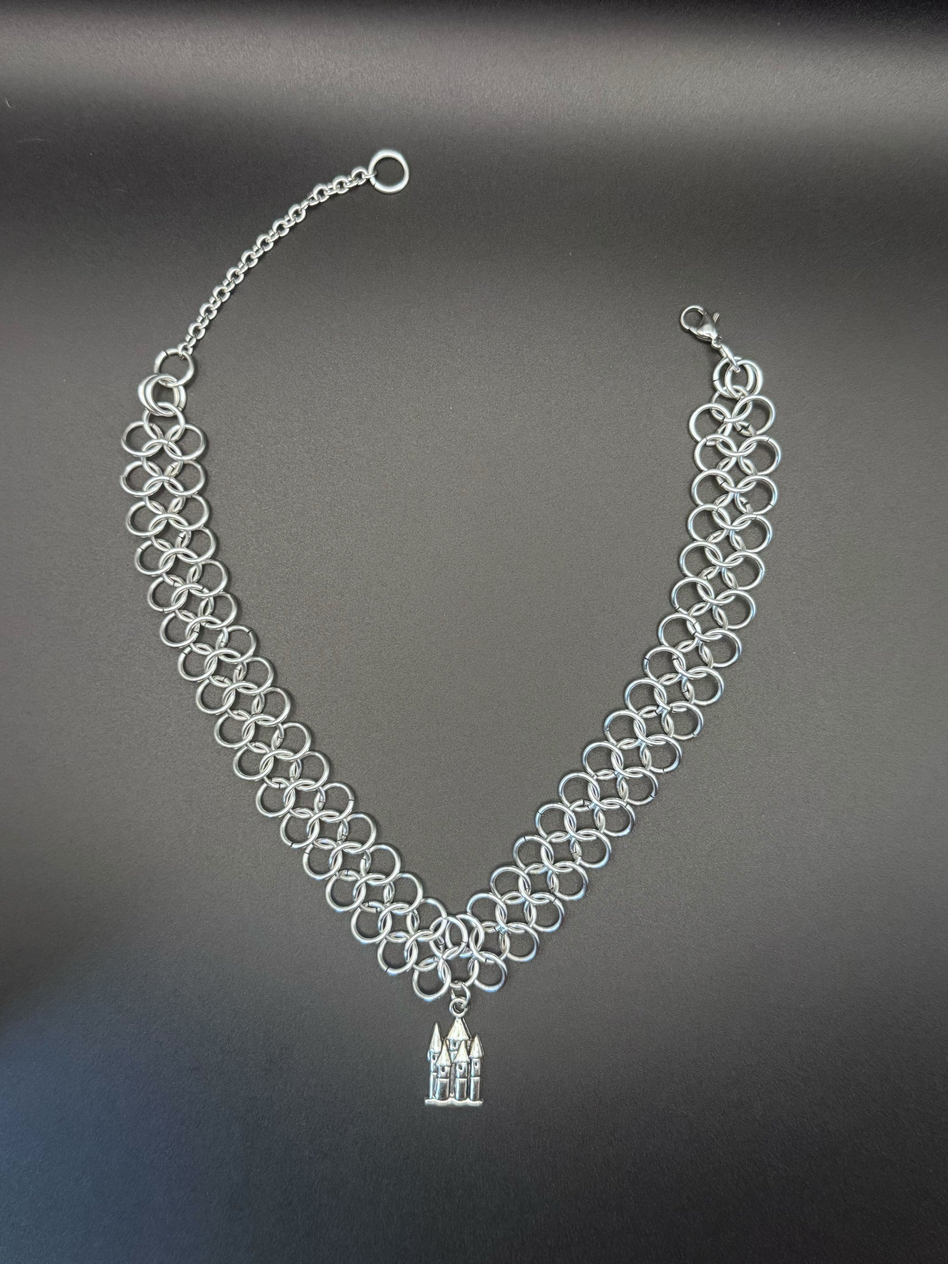 A silver chainmail choker with a medieval castle pendant.