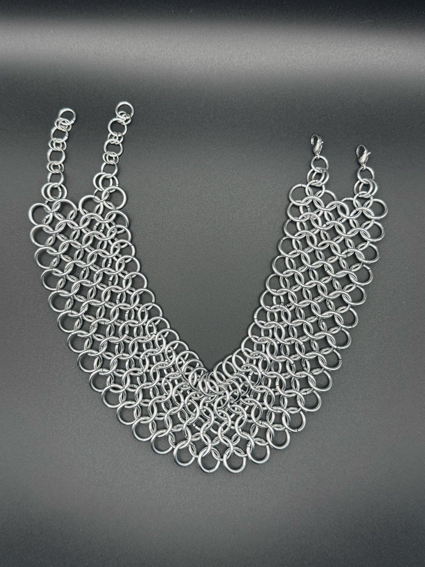 A wide silver chainmail choker with adjustable links rests on a dark background.