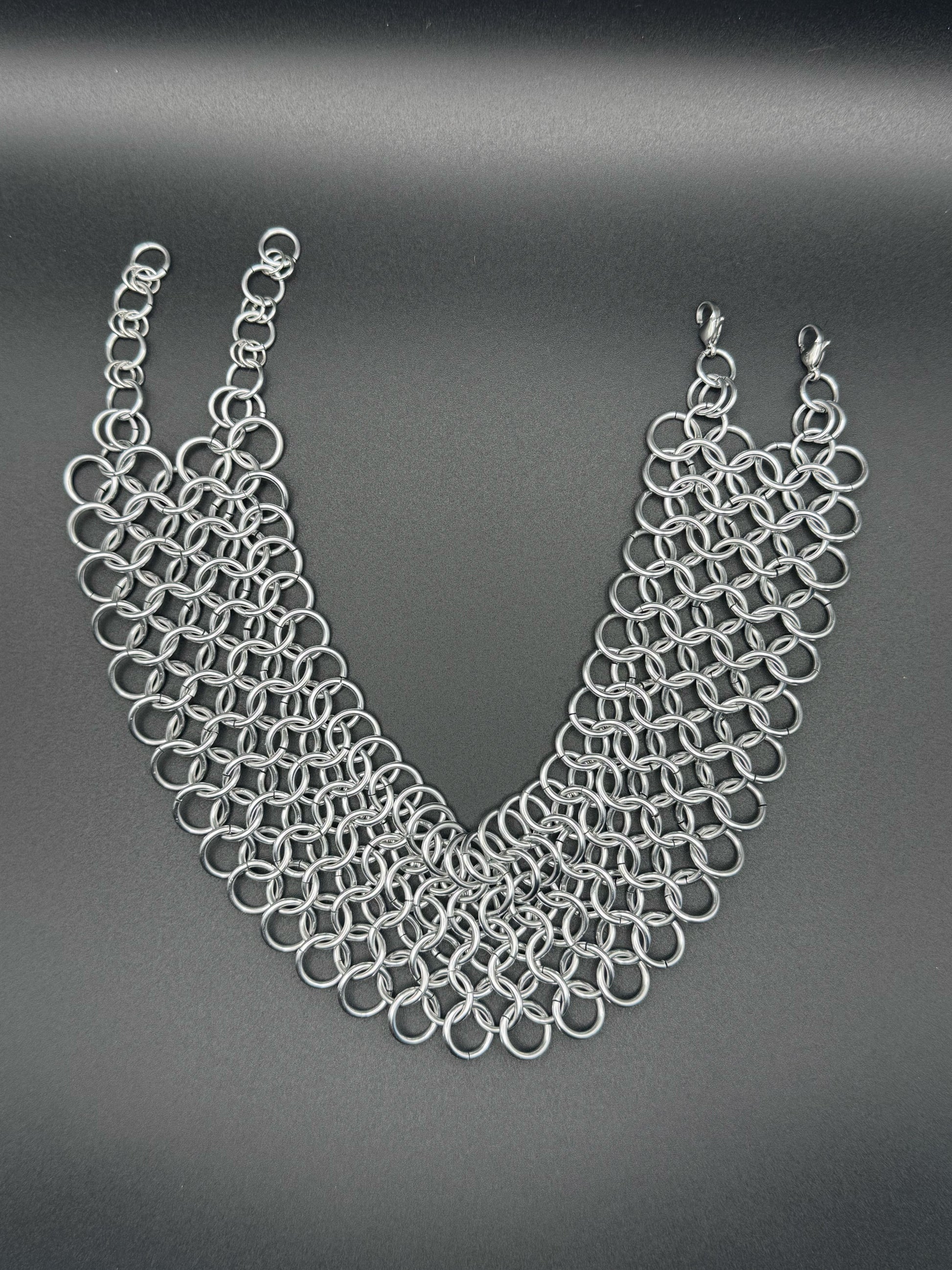 A wide silver chainmail choker with adjustable links rests on a dark background.