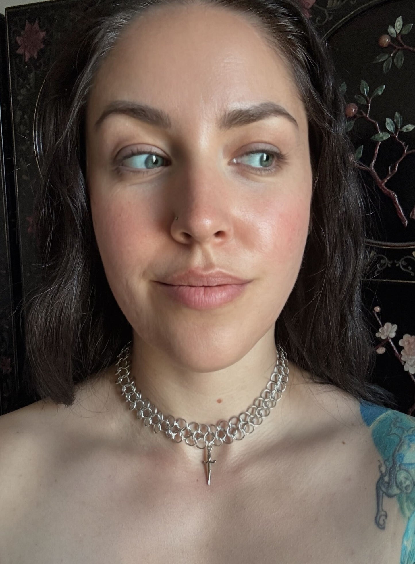Woman wearing a silver chainmail necklace with a dagger pendant with a dark background.