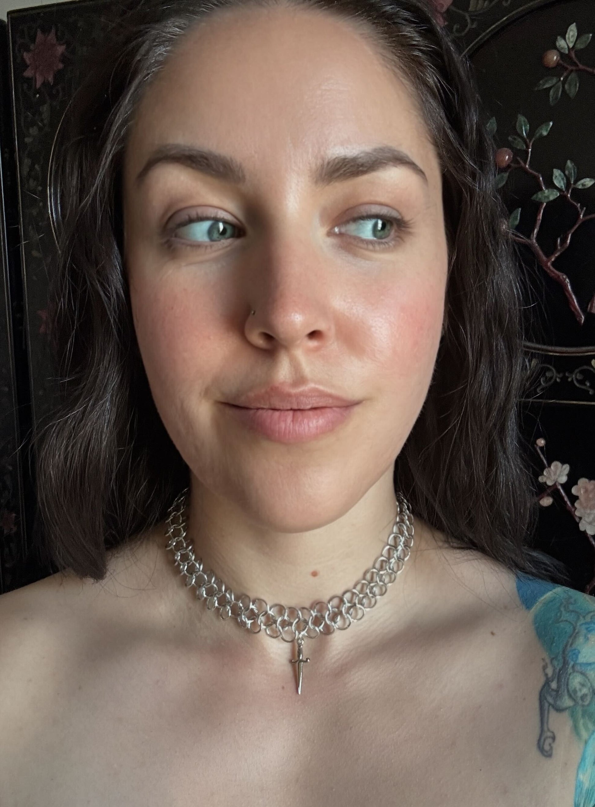 Woman wearing a silver chainmail necklace with a dagger pendant with a dark background.