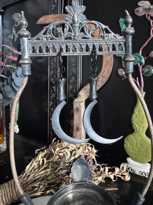 Black satin finished Sickle hoops hanging from a gothic metal stand with dried flowers in the background.