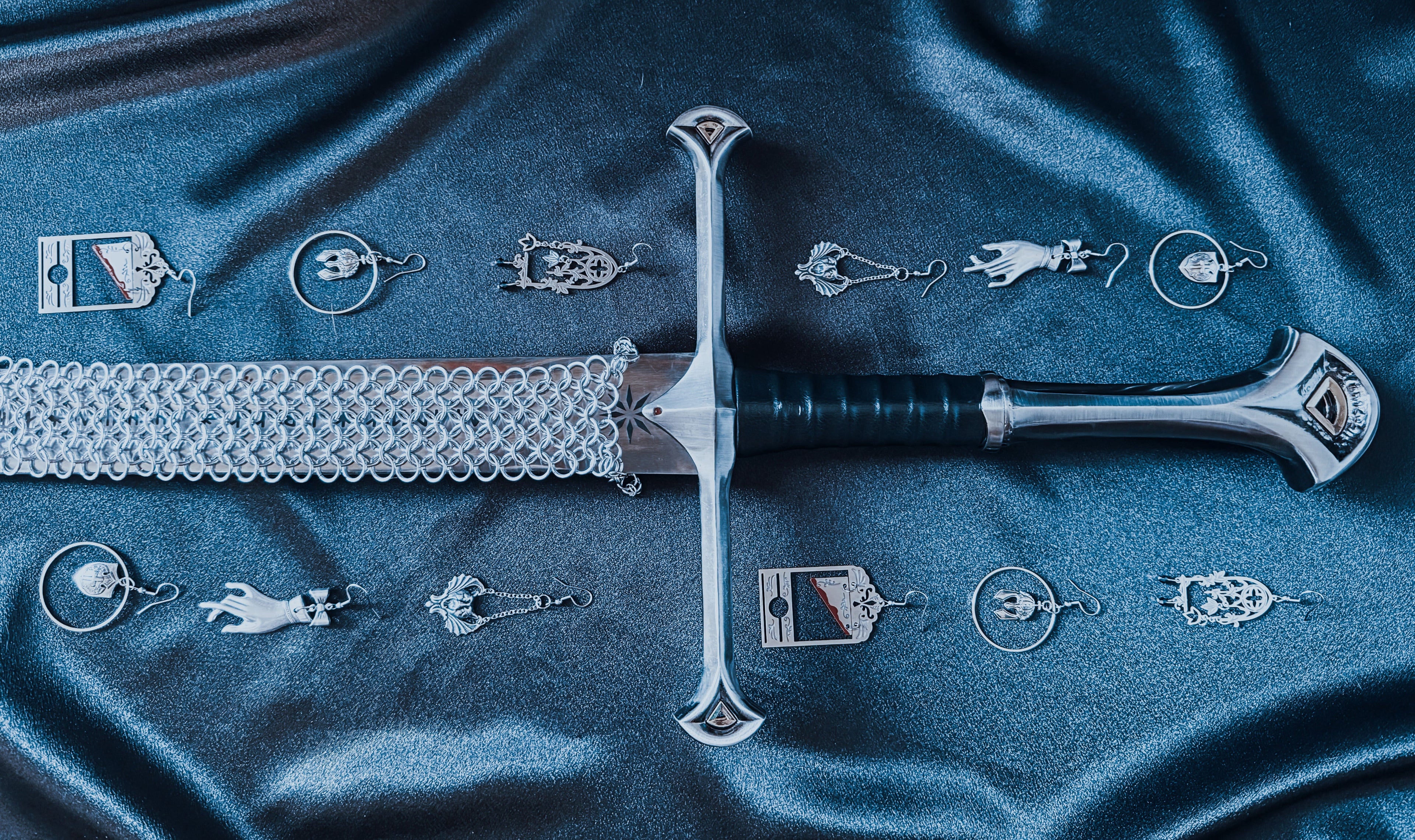 A sword rests on black satin surrounded by gothic fantasy inspired jewelry.