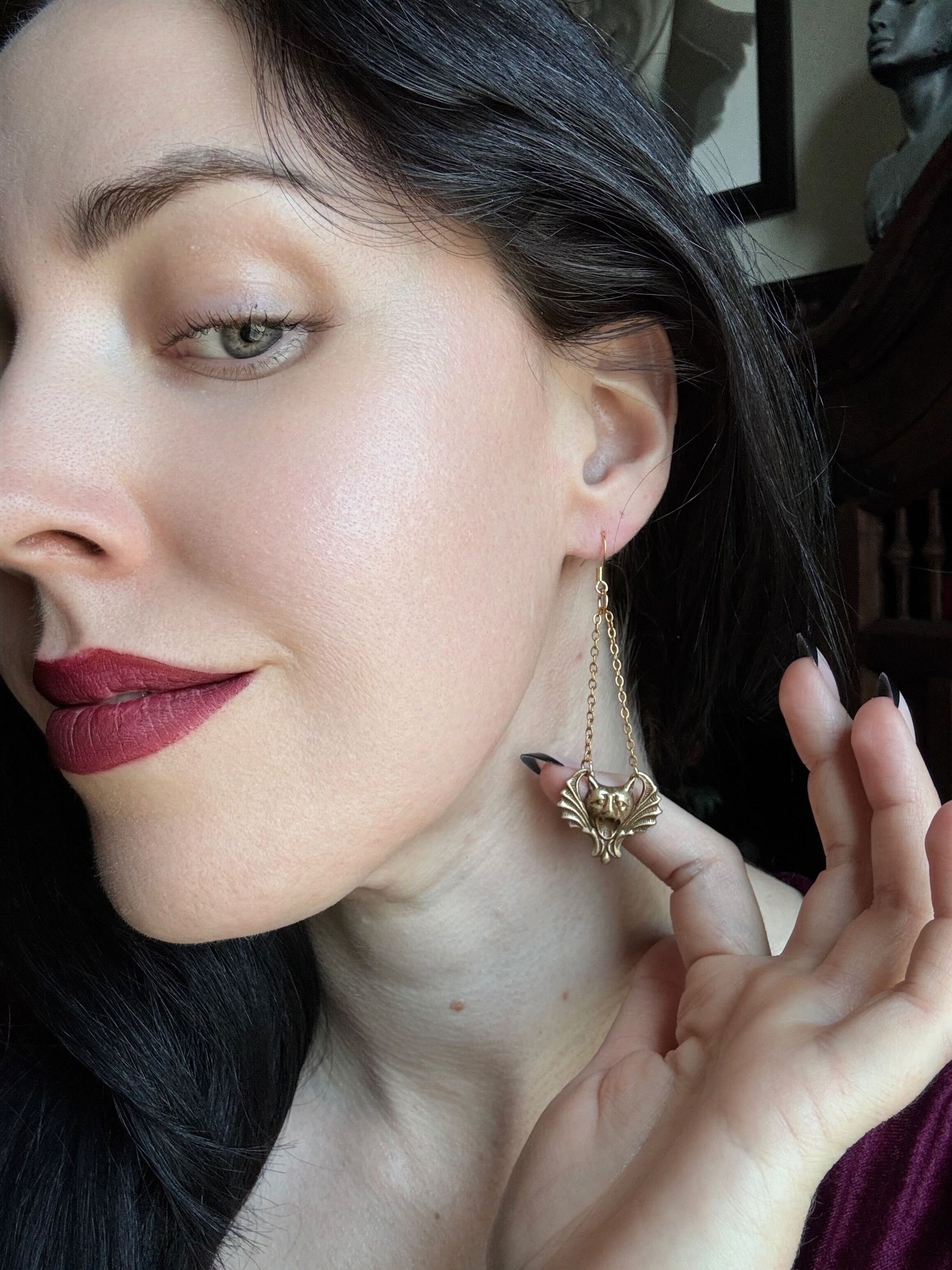 A woman wears a pair of earrings featuring brass gargoyles hanging from delicate gold chains.