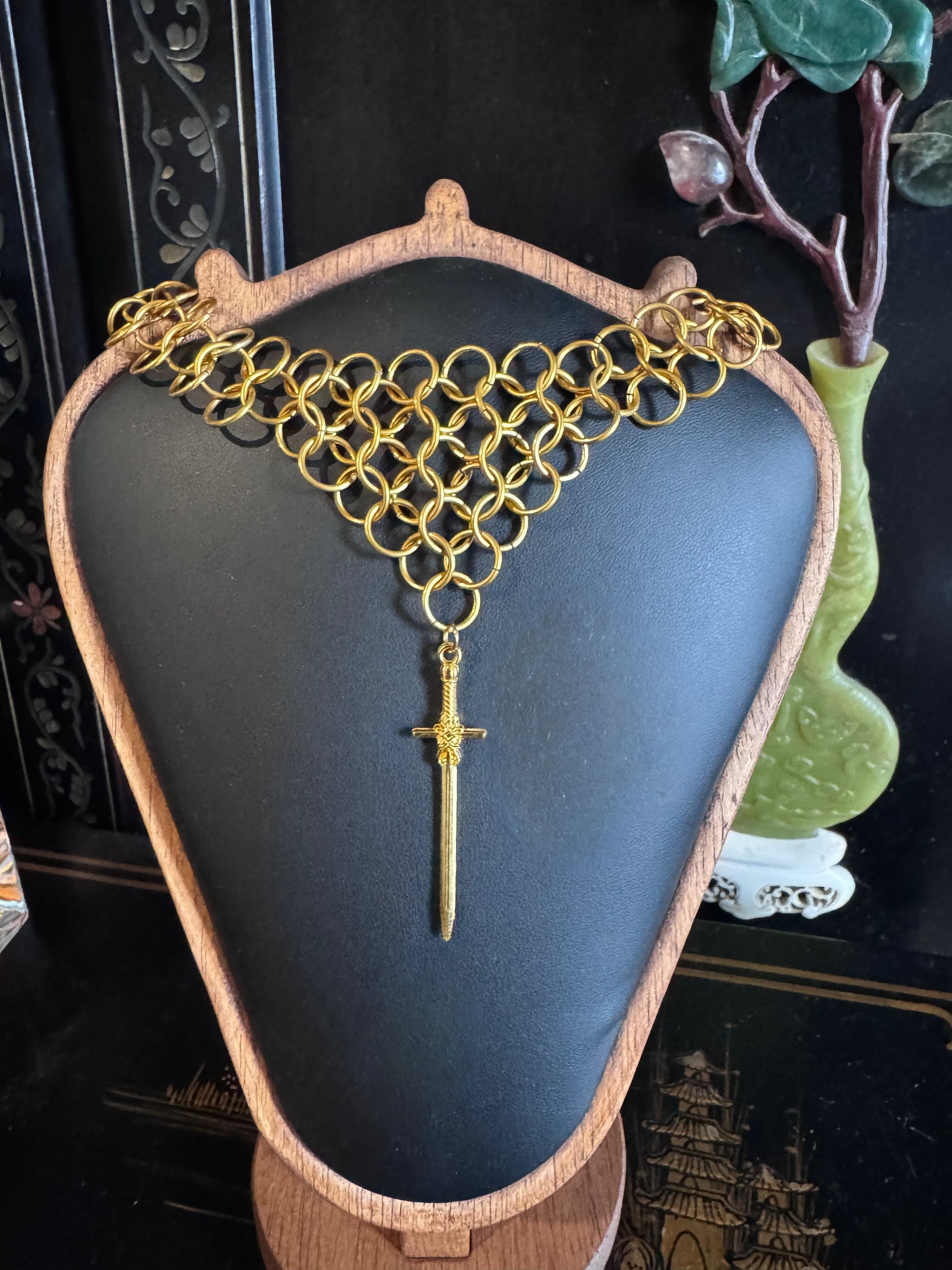 A gold chainmail necklace tapers into a point with a sword at the end.