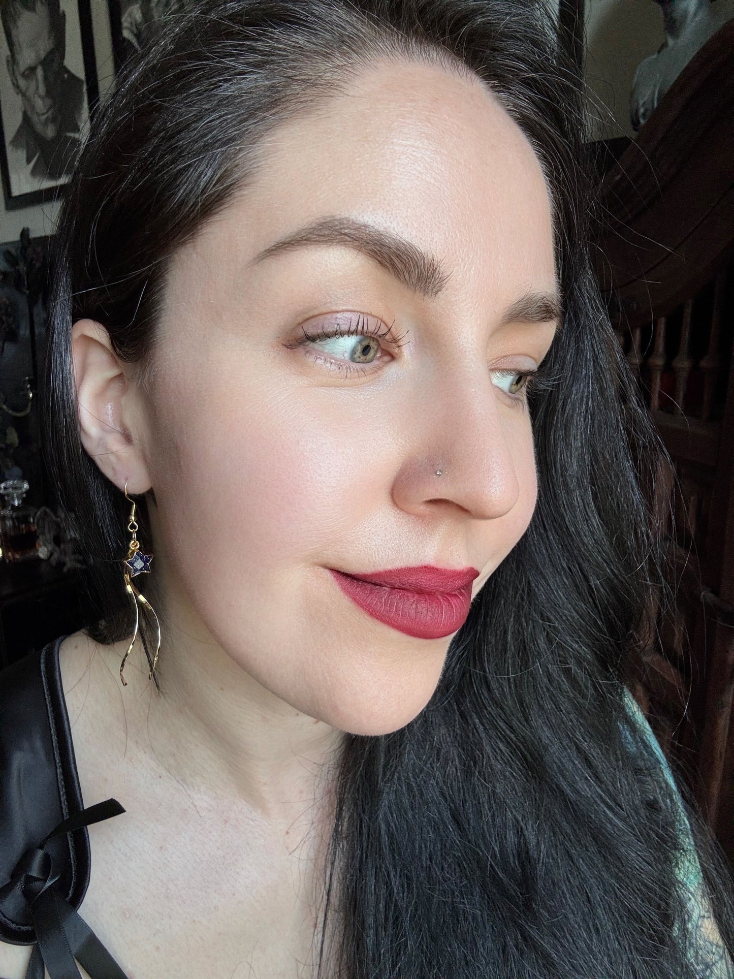 A woman wears gold plated sunstone star pendant earrings with golden threads hanging from them.