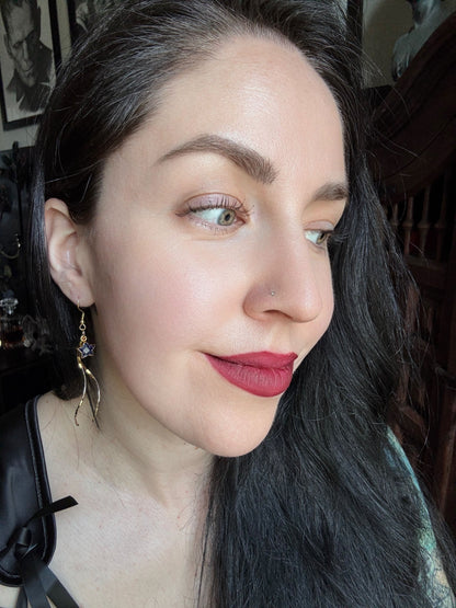 A woman wears gold plated sunstone star pendant earrings with golden threads hanging from them.