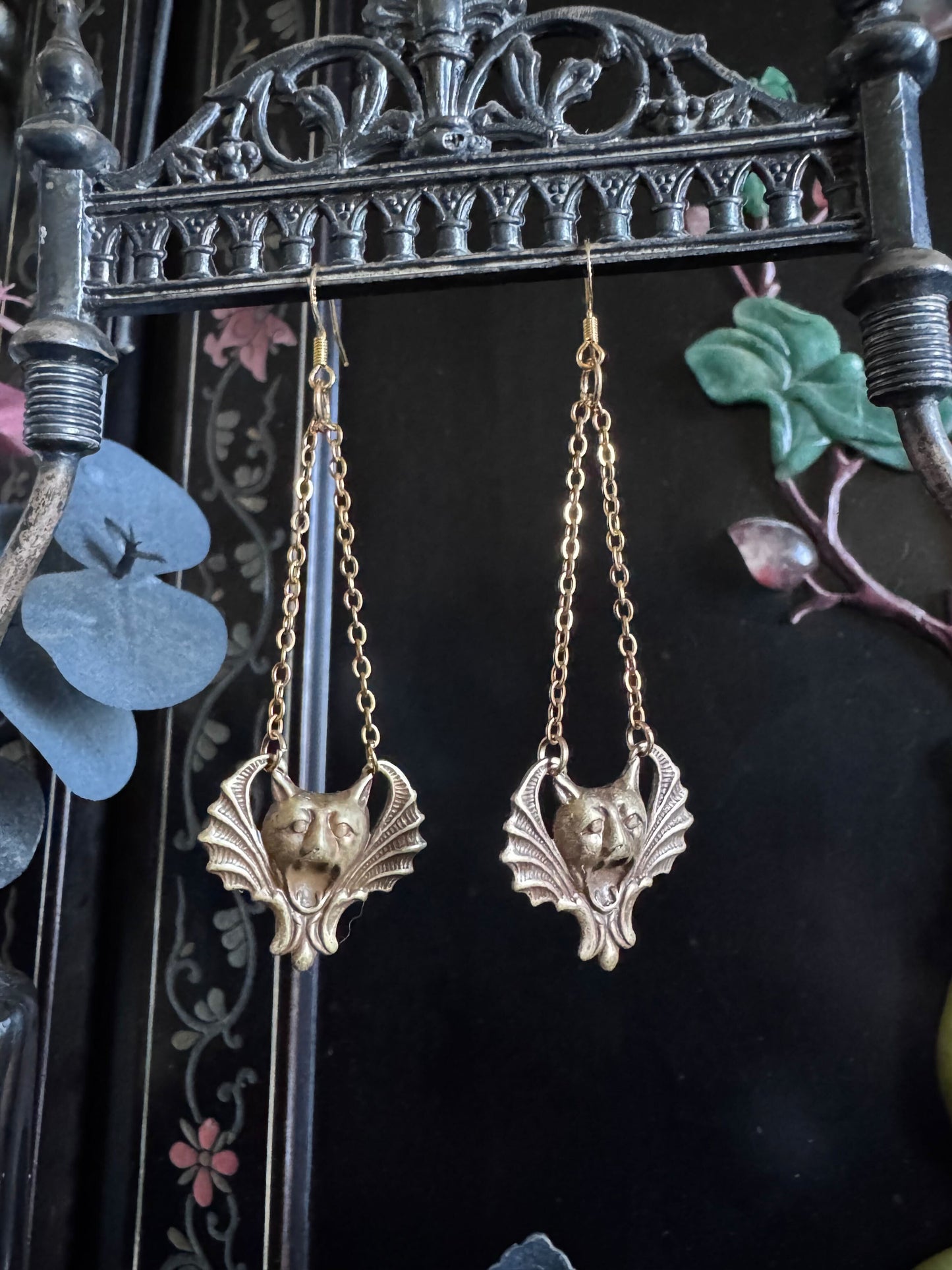 A pair of earrings feature golden hued gargoyle faces, dangling from golden chains.