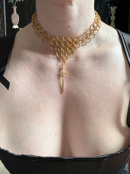 A woman wears a golden chainmail choker that tapers into a point with a sword pendant.