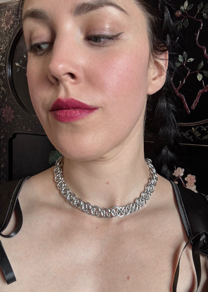 A woman wears a silver intricate chainmail necklace.