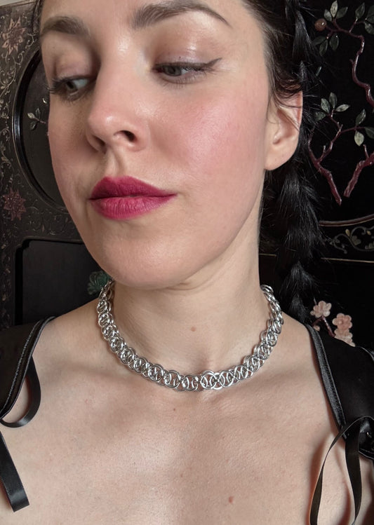 A woman wears a silver intricate chainmail necklace.