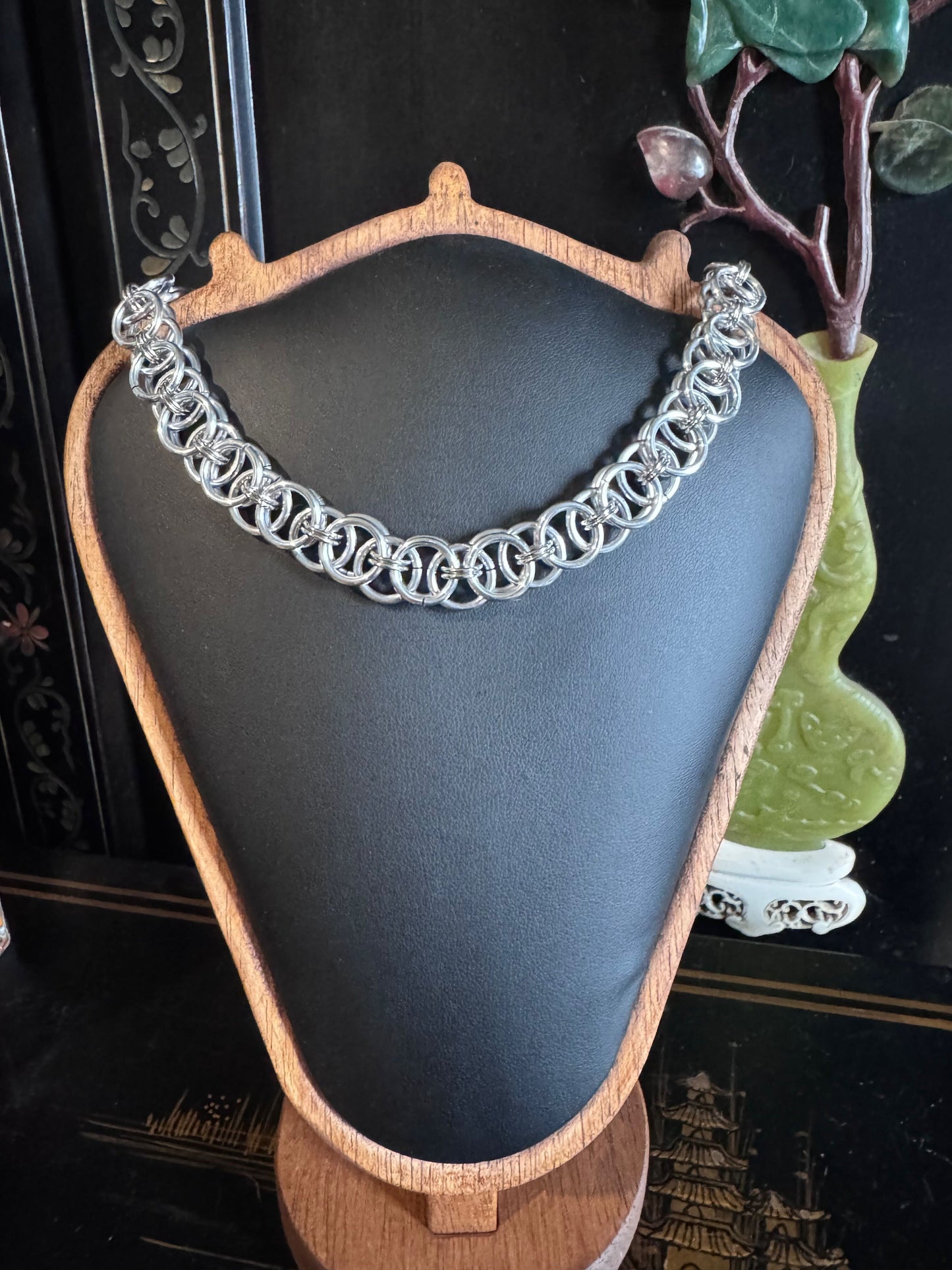 Silver intricately woven chain necklace on a mannequin bust with a dark background.