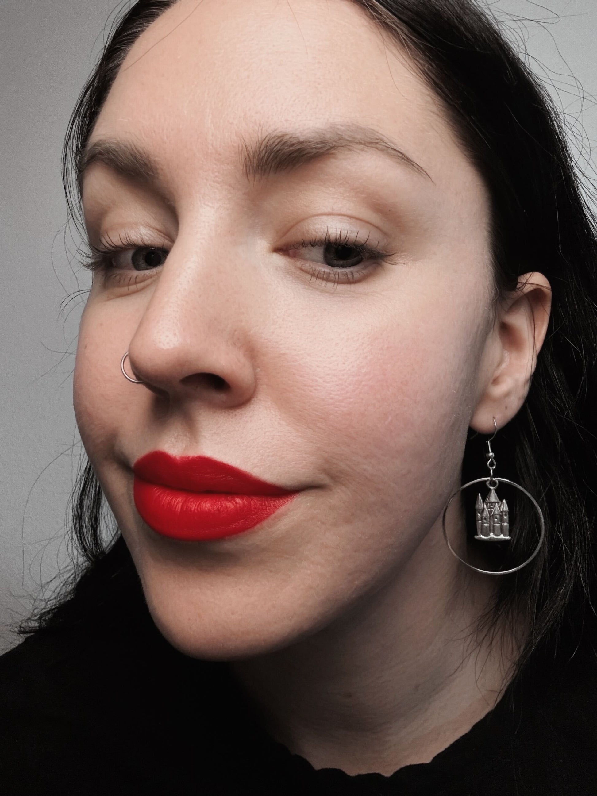 A woman wears a pair of hoop earrings featuring a medieval castle in the middle.