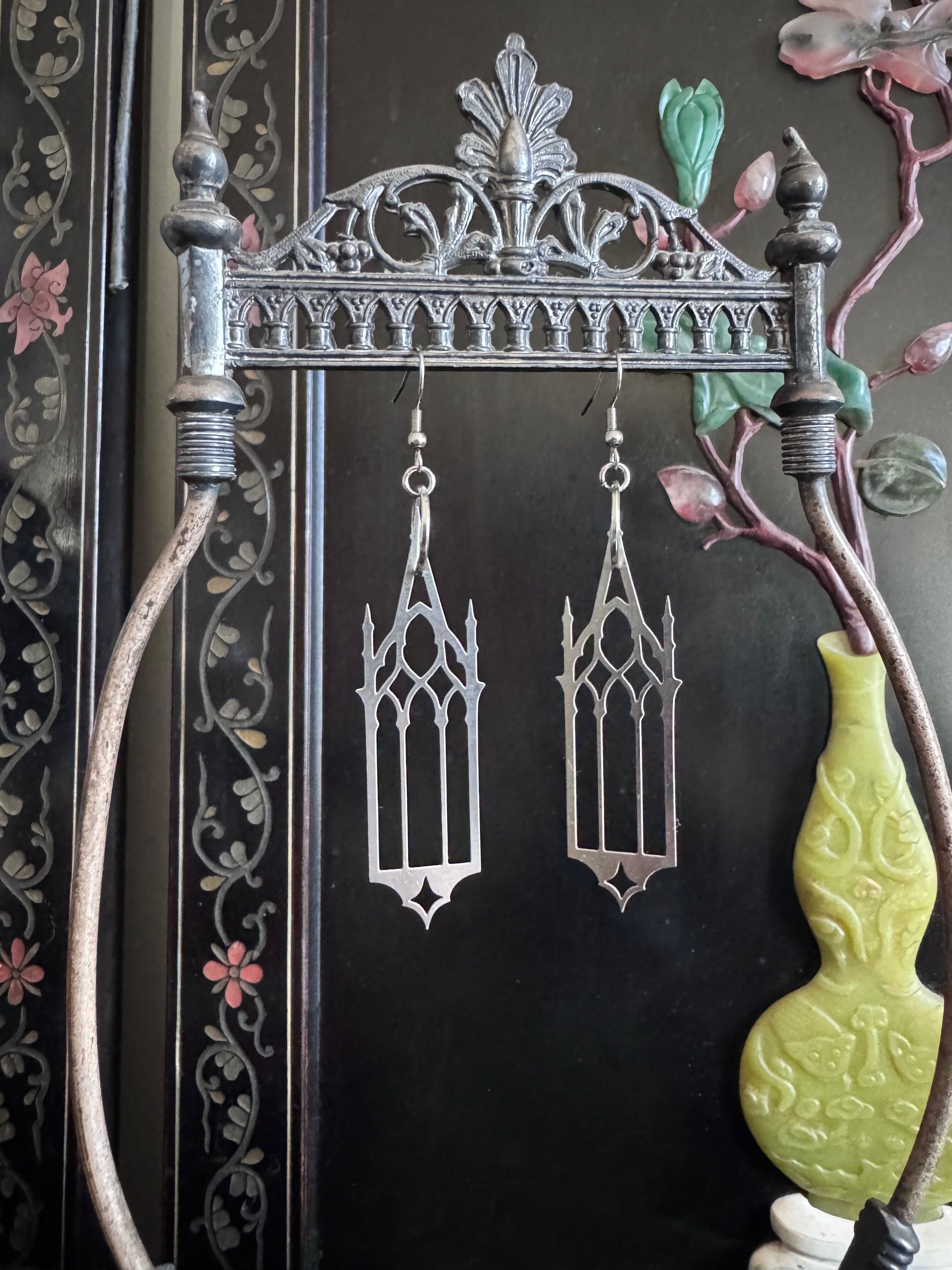 Gothic-style cathedral earrings hanging on a decorative metal stand with a dark background.