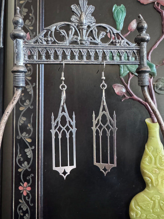 Gothic-style cathedral earrings hanging on a decorative metal stand with a dark background.