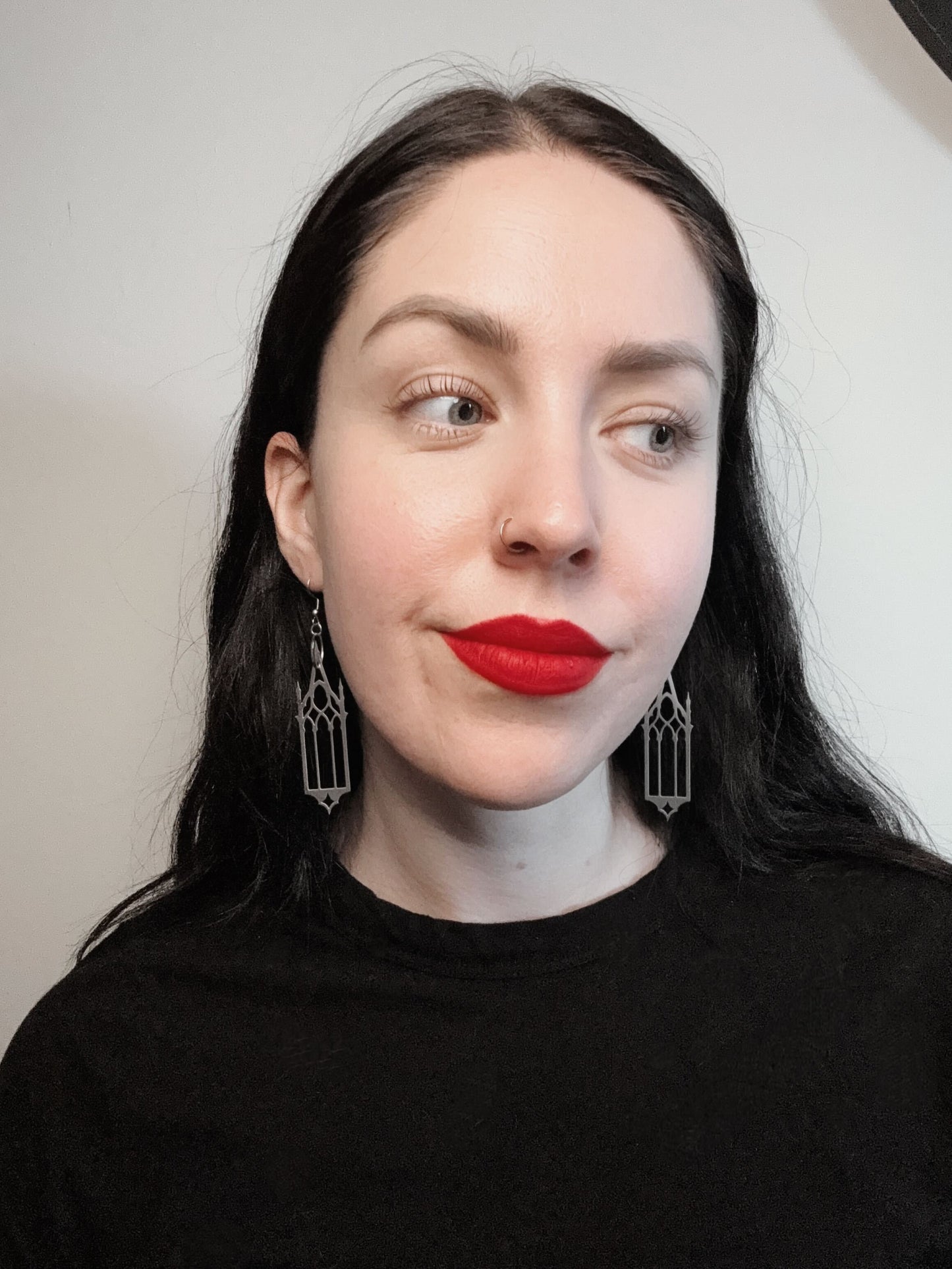 A woman wears a pair of silver earrings featuring gothic cathedral windows.