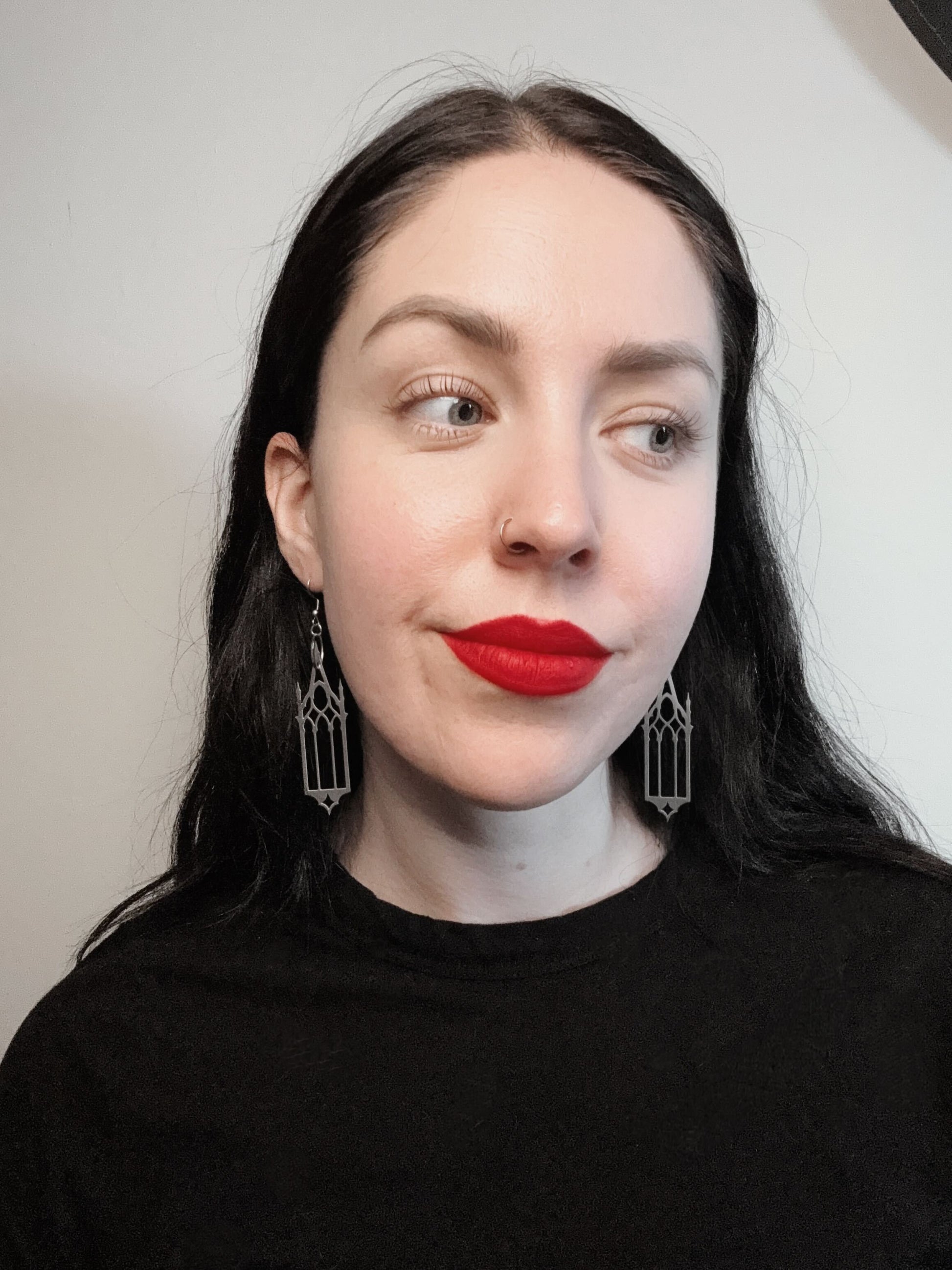 A woman wears a pair of silver earrings featuring gothic cathedral windows.