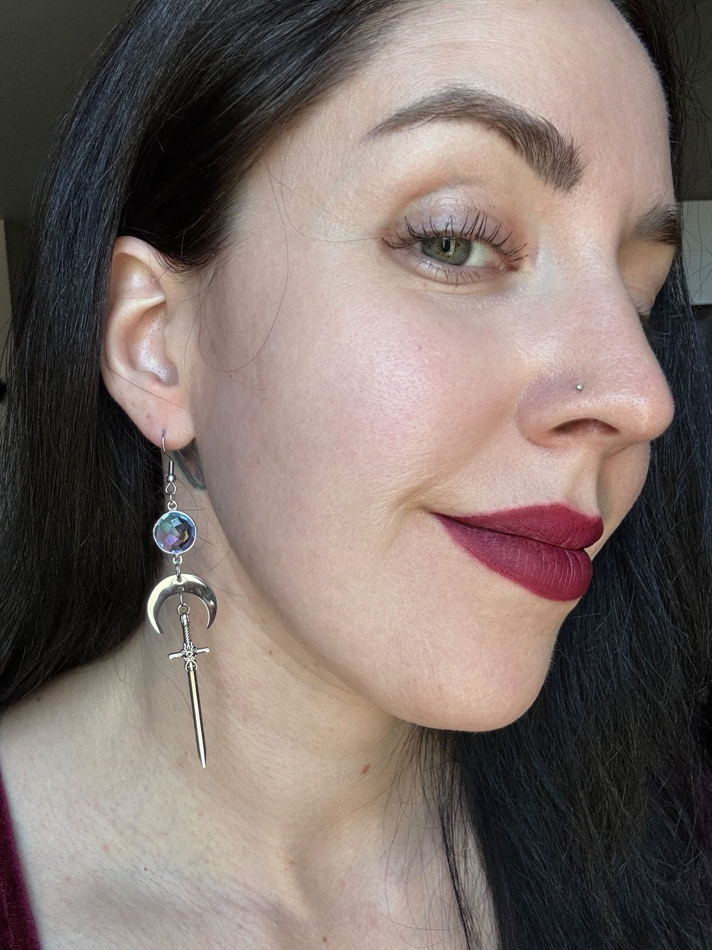 A woman wears purple blue ombre gemstone earrings with a crescent moon and sword.
