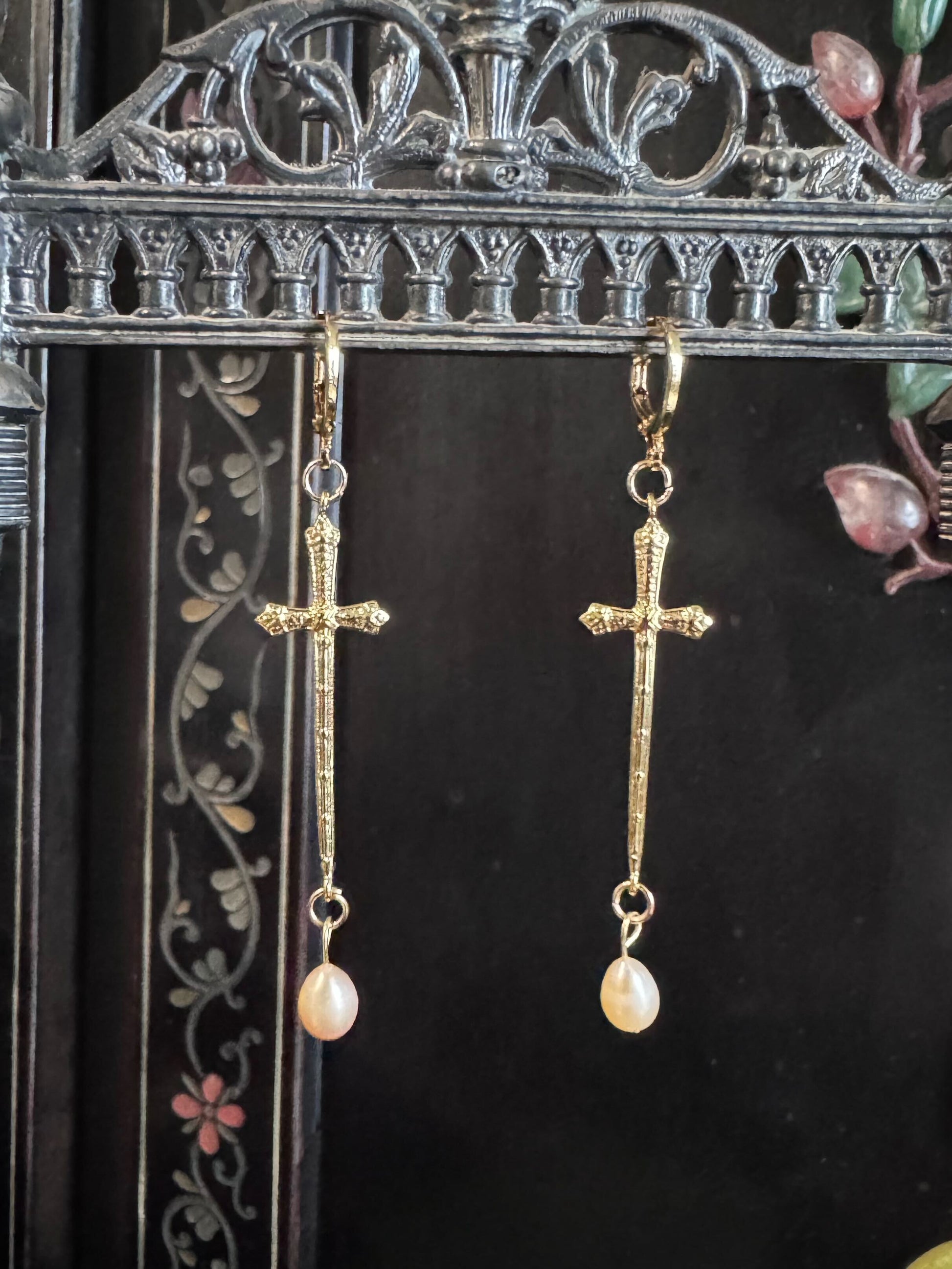 A pair of golden sword like crosses dangle from a display with freshwater pearls on the end of them.