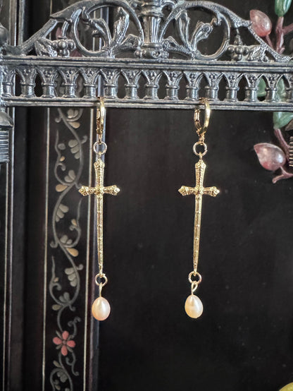 A pair of golden sword like crosses dangle from a display with freshwater pearls on the end of them.