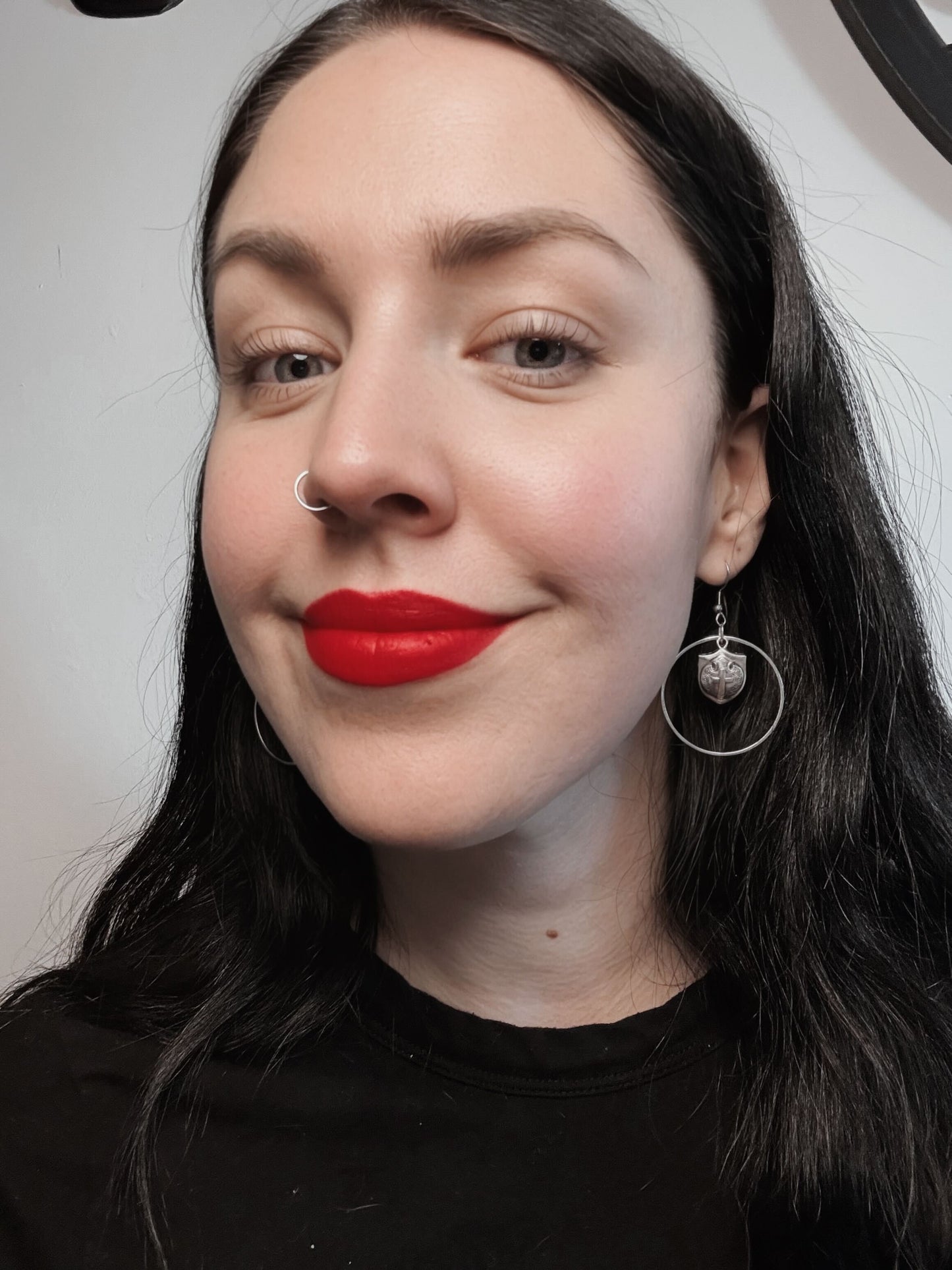 A woman wears a pair of hoop earrings with a knight's shield in the middle.