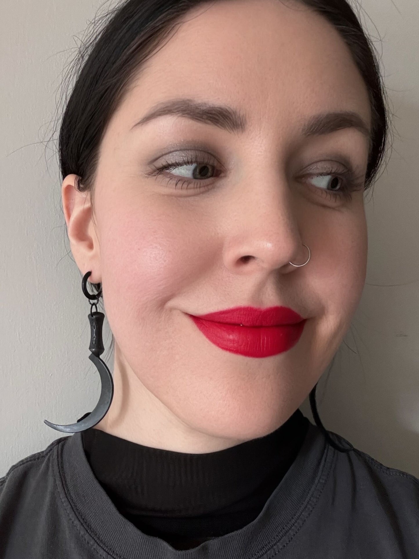 A woman wears a pair of earrings featuring large dark sickles hanging from black huggie hoops.
