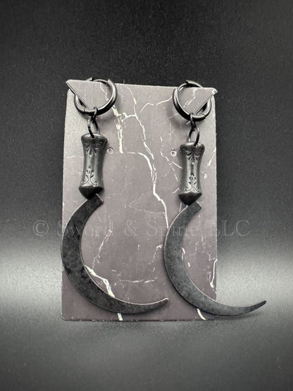 A set of black sickle/scythe earrings with black huggie clicker hoops displayed on a jewelry card.