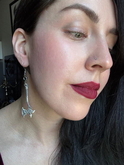 A woman wears a pair of silver finished medieval axe earrings with a fantasy aesthetic.